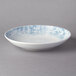A white porcelain deep coupe plate with a blue and white design.