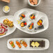 A group of Schonwald rectangular porcelain long coupe platters with food on them.