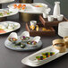 A Schonwald bone white rectangular porcelain long coupe platter on a table with sushi and other food.
