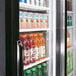 A Turbo Air black refrigerated sliding glass door merchandiser filled with drinks including bottles and cans.