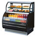 A Turbo Air black refrigerated open display case with food and drinks inside.