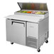 A Turbo Air stainless steel refrigerated pizza prep table with food inside.