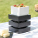 A stack of black Midnight Square Crate Risers with food on them on a table in an outdoor catering setup.