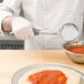 A person using a Vollrath Jacob's Pride Spoodle to serve sauce on a pizza.