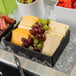 A black rectangular tray with cheese, grapes, and other food items.