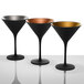 Three Stolzle black martini glasses with gold and black rims on a table.