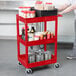 A person using a red Luxor utility cart with clear containers with red lids.