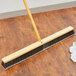 A Carlisle push broom head with gray flagged bristles on a wood floor.