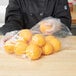 A person in a chef's coat holding a plastic bag of oranges.