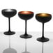 Three Stolzle Glisten black and gold coupe wine glasses on a white surface.