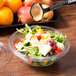 A clear Fineline plastic bowl of salad with a spoon.
