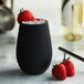 A matte black Stolzle stemless wine glass with ice and strawberries on a marble counter.