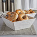 A white American Metalcraft faux slate melamine bowl filled with bagels on a counter.