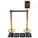 A Lancaster Table & Seating gold stanchion kit with a sign on a roped barrier.