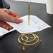A hand using a Vollrath brass check spindle to hold a piece of paper on a stand.