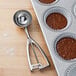 A Vollrath #12 stainless steel scoop filled with brown liquid in a cupcake tin.