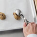 A hand using a Vollrath stainless steel oval disher to scoop cookie dough.