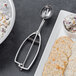 A metal spoon with a spring on a table with a plate of food and crackers.