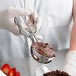 A person in gloves using a Vollrath oval stainless steel ice cream scoop to serve chocolate ice cream.
