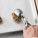 A hand using a Vollrath stainless steel scoop to scoop cookie dough.