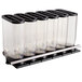 A row of clear plastic containers with black lids on a white wall shelf.