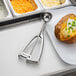 A baked potato with cheese and green onions on a plate with a Vollrath stainless steel disher.