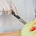 A hand in a white glove using a Mercer Culinary Japanese style carving knife to cut a watermelon.