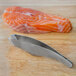 Mercer Culinary fish bone tweezers removing bones from a piece of salmon on a wooden surface.