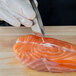 A person in white gloves using Mercer Culinary fish bone tweezers to cut a piece of salmon.