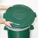 A person's hands placing a green Rubbermaid lid on a green Rubbermaid trash can.