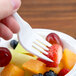 A hand holding a Dart white plastic fork over a bowl of fruit