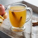 A glass mug of DaVinci Cinnamon syrup next to a glass of apple juice with cinnamon sticks.