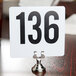 A white sign with black numbers on a stainless steel clamp-style table holder.