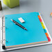 A blue Avery binder with colorful tabs open on a table with a pen and eraser on top.