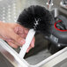 A person using a Bar Maid black and white brush to wash a glass.