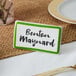 A green ceramic table tent sign with a decal border on a table with a name tag that says "Benoit Maynard"