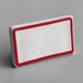 A white rectangular ceramic table tent sign with a red border and red text.