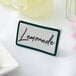 A teal ceramic table tent sign with a white border and the word "Lemonade" in white text.