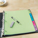 A green Avery binder with a pen and eraser on top.