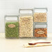 A group of glass containers with oval Kraft labels with black scalloped borders filled with different types of food.