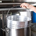 A person using a Winco aluminum stock pot with a steamer basket.