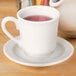 A Homer Laughlin Ameriwhite saucer holding a white cup with a red drink on it.
