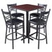 A Lancaster Table & Seating bar height table with a cherry top and black base with four black chairs with padded seats.