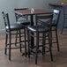 A Lancaster Table & Seating black bar height table with a reversible cherry/black top and black chairs with padded seats around it.