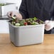 A person holding a tray of salad in a stainless steel rectangular container.
