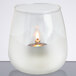 A glass candle holder with a white candle and a flame inside.