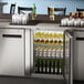 An Avantco stainless steel back bar refrigerator full of beer bottles and glasses.