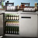 An Avantco stainless steel back bar refrigerator with beer bottles and glasses inside.
