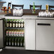 An Avantco stainless steel back bar refrigerator full of beer bottles and glasses.