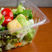 A Dart clear plastic rectangular container filled with salad, tomatoes, lettuce, and croutons.